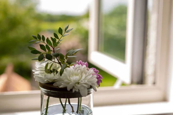 Floristry, flowers in the house, spring. A mini bouquet of flowers in a jar on the windowsill of an open window to a green garden