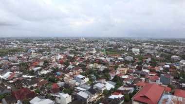 Bir banliyö mahallesinin havadan görünüşü, geniş gökyüzünün altındaki yerleşim binaları ve çatıların bulutlarla dolu olduğu çevreyi ortaya çıkarır..
