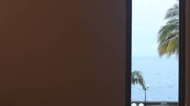 Deniz kıyısındaki ağaçlar otel penceresinin arkasından görülebilir. Tırnak işareti yazmak için boşluk
