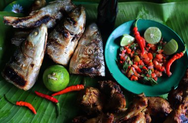 Muz yaprakları üzerinde servis edilen ızgara balık ve acı biber sosunun yakın plan portresi.