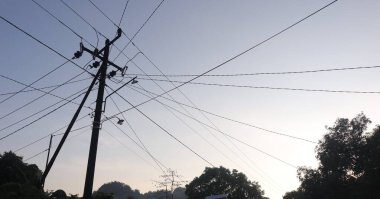 Elektrik direklerindeki elektrik kablolarından oluşan bir ağ ve öğleden sonra açık mavi bir gökyüzü.