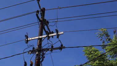 Elektrik direklerindeki elektrik kablolarından oluşan bir ağ ve öğleden sonra açık mavi bir gökyüzü.