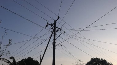 Elektrik direklerindeki elektrik kablolarından oluşan bir ağ ve öğleden sonra açık mavi bir gökyüzü.