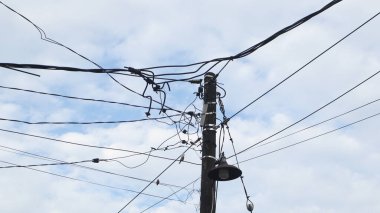Elektrik direklerindeki elektrik kablolarından oluşan bir ağ ve öğleden sonra açık mavi bir gökyüzü.