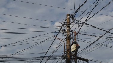 Elektrik direklerindeki elektrik kablolarından oluşan bir ağ ve öğleden sonra açık mavi bir gökyüzü.