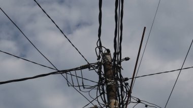 Elektrik direklerindeki elektrik kablolarından oluşan bir ağ ve öğleden sonra açık mavi bir gökyüzü.
