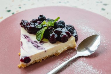 Üzerinde nane yaprağı olan seramik tabakta yaban mersinli cheesecake..