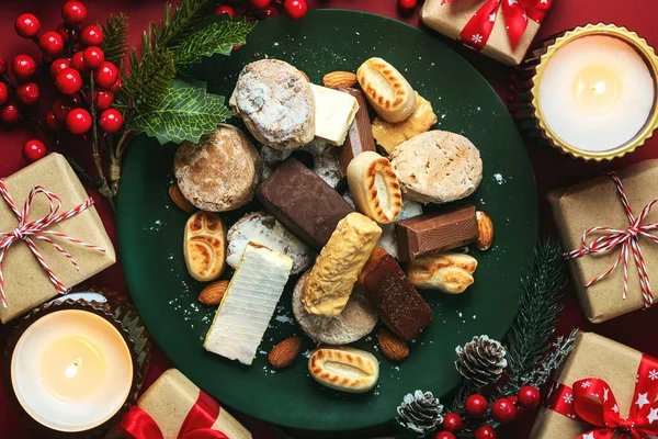 Top view of Nougat christmas sweet,mantecados and polvorones with christmas ornaments on a plate over a red background. Assortment of christmas sweets typical in Spain