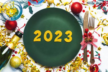 Mutlu yıllar 2023. Noel yemeği için tabakta altın numaralar 2023 noel süsleri ve Noel masa örtüsünün üstünde şampanya şişesiyle. Yeni yıl kutlamaları konsepti
