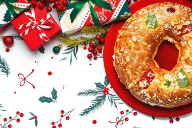 Roscon de Reyes 'in üst görüntüsü. Kremalı ve noel süsleri kırmızı bir tabakta, masa örtüsünün üzerinde. Krallar Günü konsepti İspanyolca üç papaz pastası. Noel için tipik İspanyol tatlısı.
