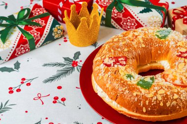 Kremalı Roscon de Reyes ve noel masa örtüsünün üstünde kırmızı bir tabakta Noel süsleri. Krallar Günü konsepti İspanyolca üç papaz pastası. Noel için tipik İspanyol tatlısı.