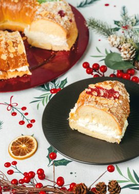 Kremalı Roscon de Reyes ve noel masa örtüsünün üstünde kırmızı bir tabakta Noel süsleri. Krallar Günü konsepti İspanyolca üç papaz pastası. Noel için tipik İspanyol tatlısı.