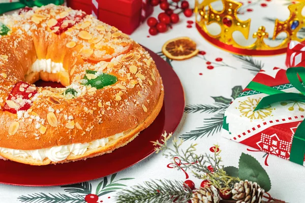 stock image Roscon de reyes with cream and christmas ornaments on a red plate over christmas tablecloth. Kings day concept spanish three kings cake.Typical spanish dessert for Christmas