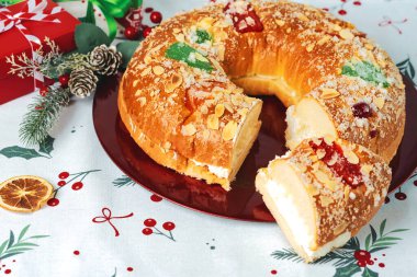 Kremalı Roscon de Reyes ve noel masa örtüsünün üstünde kırmızı bir tabakta Noel süsleri. Krallar Günü konsepti İspanyolca üç papaz pastası. Noel için tipik İspanyol tatlısı.