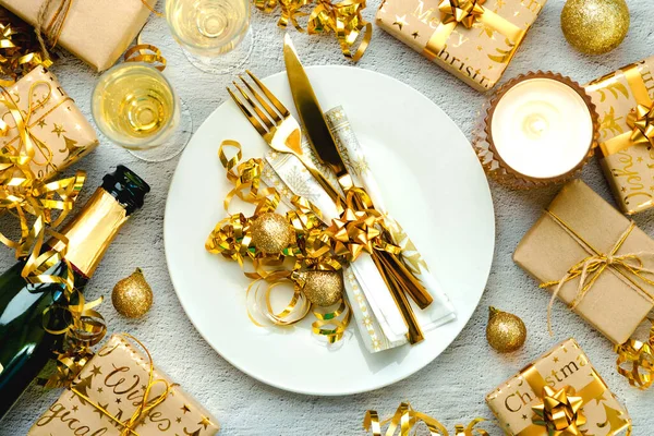 Christmas dinner concept. Top view of golden cutlery on a plate with christmas ornament and champagne bottle over white background. Christmas concept background