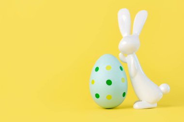 Mutlu Paskalyalar. Paskalya yumurtasının, sarı arkaplana karşı metin için fotokopi alanı olan paskalya tavşanının yanına yakın plan.