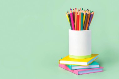 Beyaz kavanoza renkli kalemler ve yeşil arkaplana karşı metin için yeri olan defterler. Okul konseptine dönelim.
