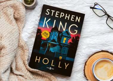 Amerikalı romancı Stephen King 'in beyaz bir battaniyenin üzerinde kahve ve bardakla yazdığı İspanyolca Holly kitabının yakın çekimi.