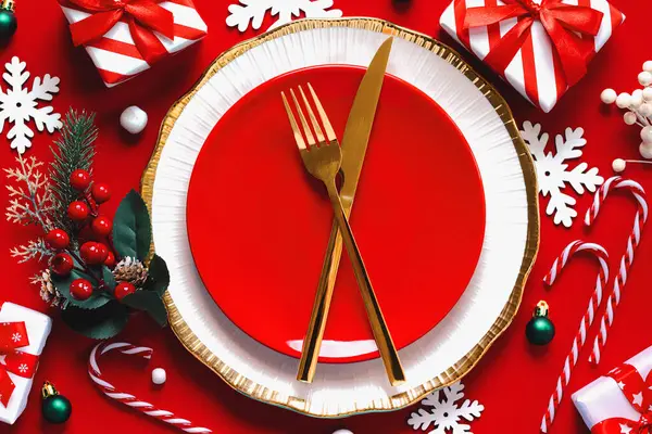Christmas dinner concept. Top view of golden cutlery on a red plate with christmas ornaments over red background. Christmas concept background