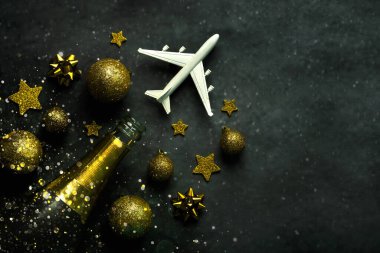 Noel konsepti geçmişi. Şampanya şişesi, noel baloları, ışıltılı parıltı ve gri arka planda mesaj için yeri olan uçak. Noel yolculuğu konsepti