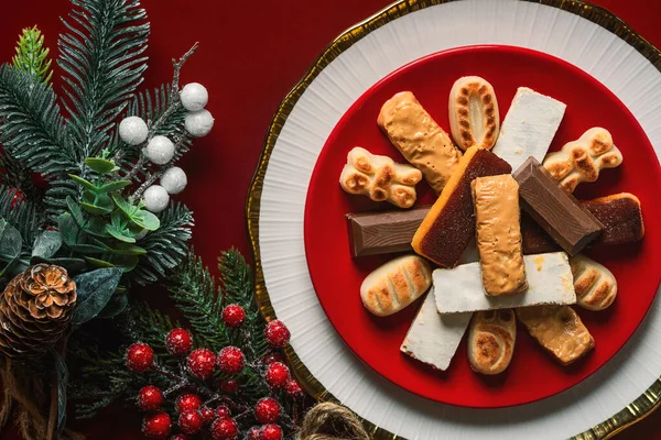 Top view of Nougat christmas sweet with christmas ornaments on a plate over a red background. Assortment of christmas sweets typical in Spain