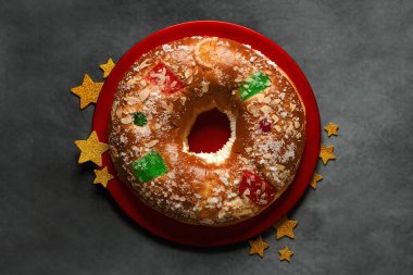 Kırmızı tabakta altın yıldızlı Roscon de Reyes manzarası. Krallar Günü konsepti İspanyolca. Gri arka planda üç papaz pastası. Krallar Günü konsepti İspanyolca üç kralın pastası