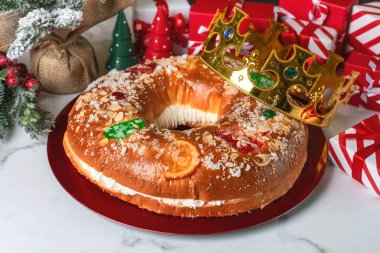 Kremalı Roscon de Reyes ve mermer bir masada kırmızı bir tabakta noel süsleri. Krallar Günü konsepti İspanyolca üç papaz pastası. Noel için tipik İspanyol tatlısı.