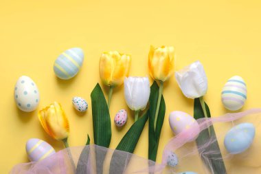 Mutlu Paskalyalar. Renkli Paskalya yumurtası ve sarı arka planda beyaz ve sarı laleler.