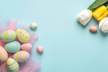 Mutlu Paskalyalar. Renkli paskalya yumurtaları ve laleleri mavi arkaplan üzerindeki metin için kopyalama alanı ile boyanmış