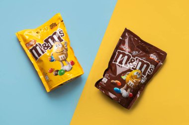Mavi ve sarı arkaplan üzerinde M & M çikolata ve fıstık paketleri yakın çekim. İllüstrasyon Editörü