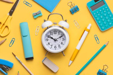 Okul malzemeleri ile kompozisyonun üst görüntüsü ve sarı arkaplanda yazı için yeri olan beyaz alarmlı saat. Okul konseptine dönelim.
