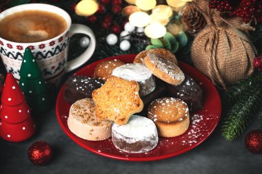 Different Spanish Christmas shortbreads or mantecados and polvorones on a red plate with christmas ornaments on a grey tablecloth. Assortment of christmas sweets typical in Spain clipart