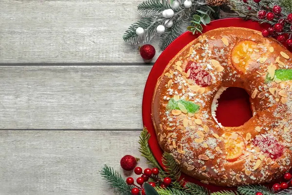 Kırmızı bir tabakta kırmızı böğürtlen dalları, noel topları ve ahşap bir masada yazı için yer olan Roscon de Reyes 'in üst görüntüsü. Krallar Günü konsepti İspanyolca üç papaz keki