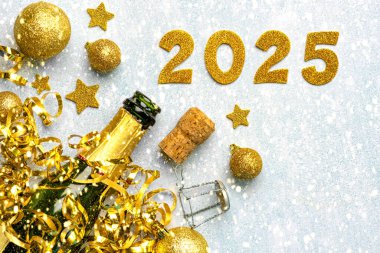 İçinde altın noel baloları olan bir şişe şampanya, altın yıldızlar ve karlı bir arka planda 2025 'lik altın rakamlar. Yeni yıl kutlamaları konsepti