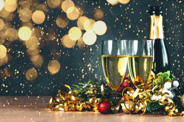 Bottle of champagne with crystal glasses, golden streamers,christmas lights and space for text on a wooden table. New years eve celebration concept background
