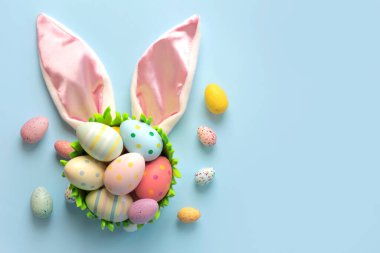 Mutlu Paskalyalar. Renkli paskalya yumurtaları tavşan kulakları üzerine boyanmış ve mavi arkaplan üzerindeki metin için kopya alanı var.