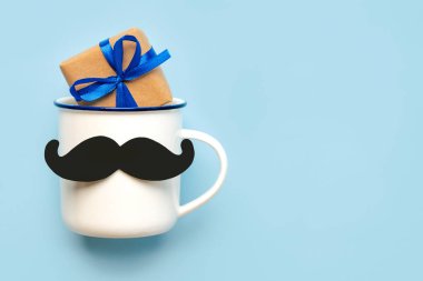 Babalar Günün kutlu olsun. Takma bıyıklı kahve fincanının üst görüntüsü ve mavi arkaplanda metin için kopya alanı olan hediye kutusu