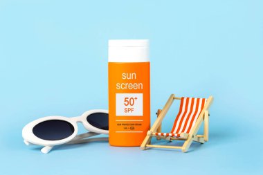 Closeup of white sunglasses, beach deck chair and bottle of sunscreen with 50+ written on it on a blue background. Summer holidays concept