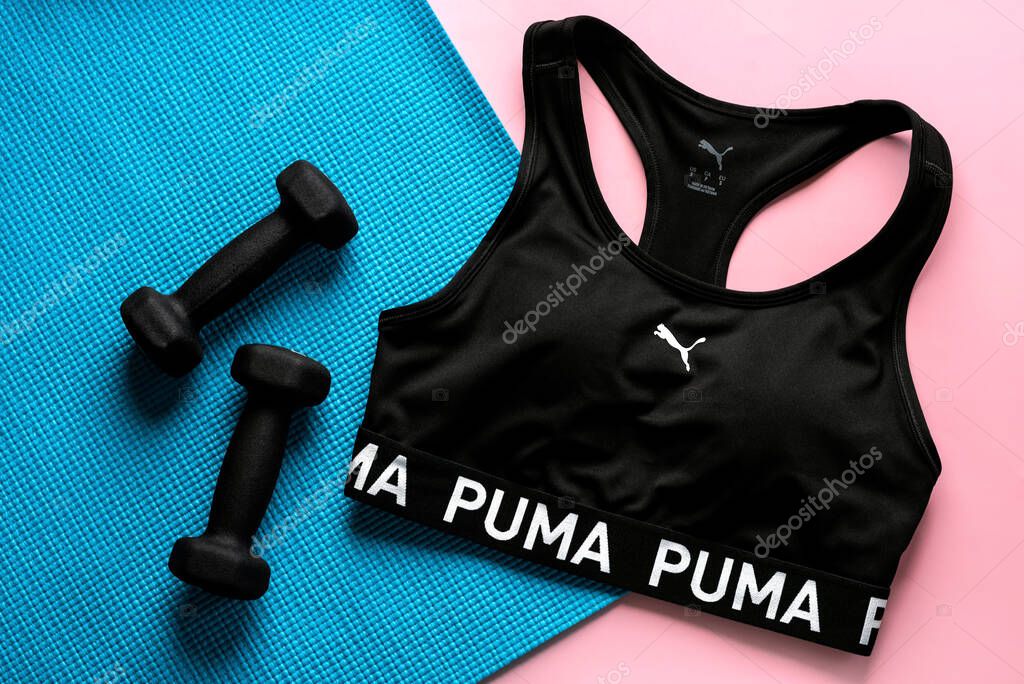 Top view of Puma sports bra,black dumbbells and fitness mat over pink background. Illustrative editorial