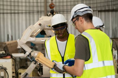 Robot mühendisleri fabrika deposunda modern robotik kolun bakımı üzerinde çalışıyorlar.