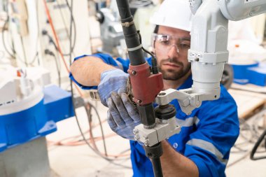 Robot mühendisi fabrika deposunda modern robotik kolun bakımı üzerinde çalışıyor.