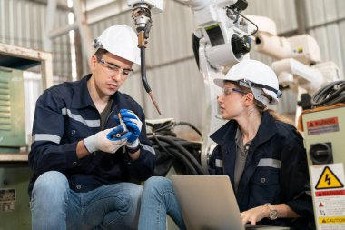 Robot mühendisleri fabrika deposunda modern robotik kolun bakımı üzerinde çalışıyorlar.