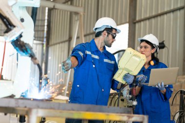 Robot mühendisleri fabrika deposunda modern robotik kolun bakımı üzerinde çalışıyorlar.