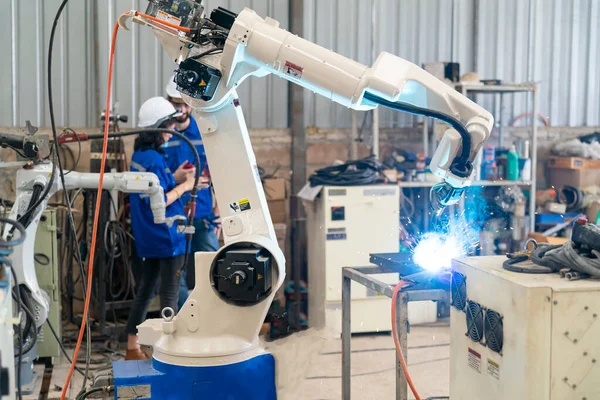 Robot mühendisleri fabrika deposunda modern robotik kolun bakımı üzerinde çalışıyorlar.