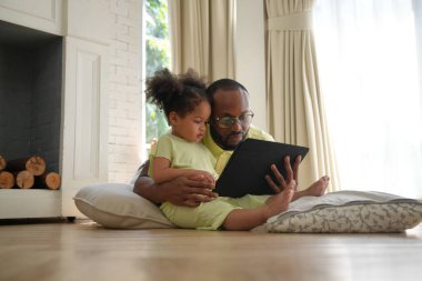 Afro-Amerikan baba ve kızı evde dijital tablet kullanıyorlar.