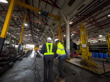 Üniformalı ve kasklı bir erkek işçi fabrikada vinç kullanıyor. Endüstriyel üretim, metal mühendisliği, güç makineleri üretimi