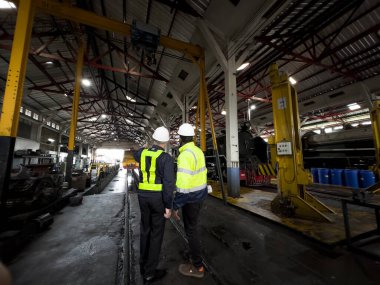 Üniformalı ve kasklı bir erkek işçi fabrikada vinç kullanıyor. Endüstriyel üretim, metal mühendisliği, güç makineleri üretimi