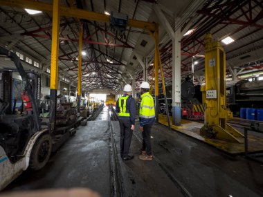 Üniformalı ve kasklı bir erkek işçi fabrikada vinç kullanıyor. Endüstriyel üretim, metal mühendisliği, güç makineleri üretimi