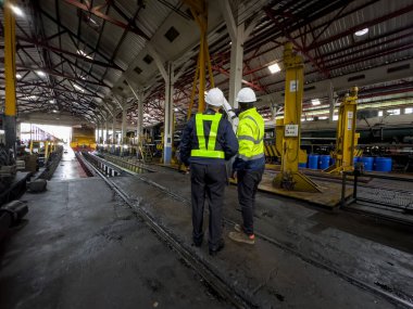 Üniformalı ve kasklı bir erkek işçi fabrikada vinç kullanıyor. Endüstriyel üretim, metal mühendisliği, güç makineleri üretimi