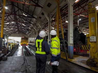 Üniformalı ve kasklı bir erkek işçi fabrikada vinç kullanıyor. Endüstriyel üretim, metal mühendisliği, güç makineleri üretimi